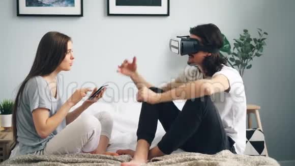 当女孩使用平板电脑时身穿vr护目镜双臂在床上移动的快乐男人视频的预览图