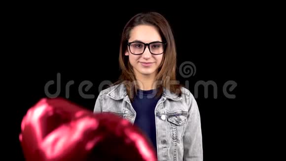 年轻女子面前心形气球起飞女孩微笑着站在黑色的背景上气球视频的预览图
