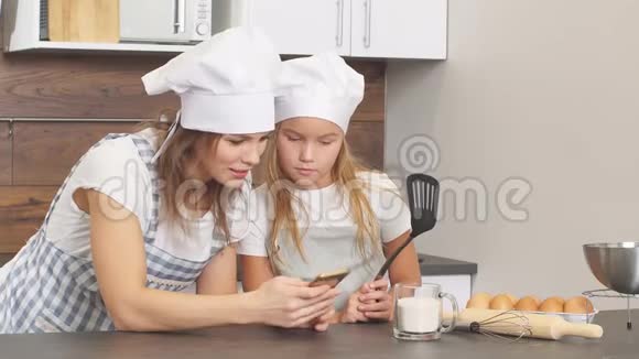 穿着围裙的幸福家庭看看智能手机屏幕看看美味的蛋糕配方视频的预览图