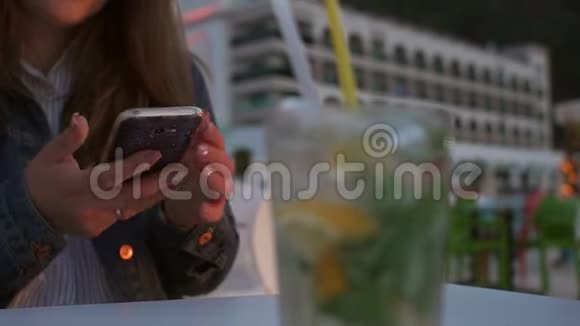 一个女孩在咖啡馆里用手机特写靠近一个模糊的玻璃和一个莫吉托视频的预览图