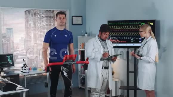 两名混合赛医生讨论运动员在运动实验室做跑步机测试的心电图数据视频的预览图