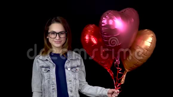 一个年轻的女孩站着心形的气球女人手里拿着黑色背景的氦球视频的预览图