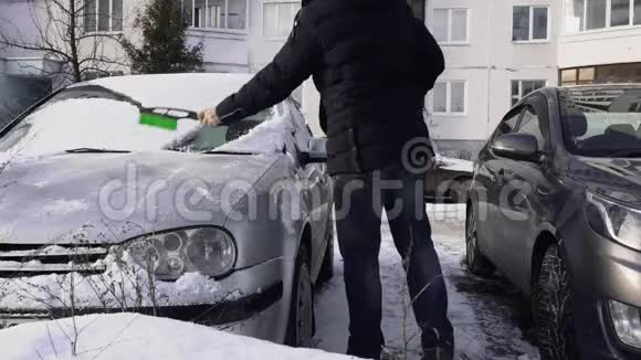 冬天白天在院子里的停车场里人们从雪地上清洁汽车的挡风玻璃或挡风玻璃又坏又冷视频的预览图