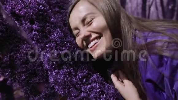紫罗兰童话森林穿着淡紫色夹克的快乐女孩抚摸着树上柔软厚厚的紫色苔藓微笑着幻想视频的预览图
