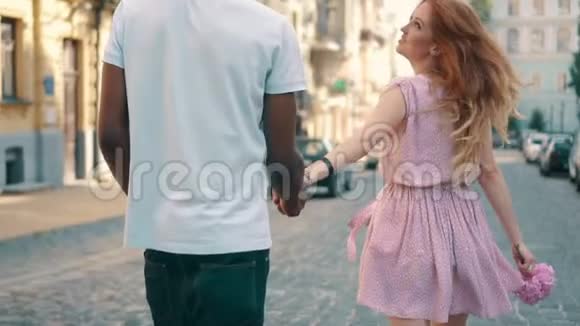 年轻快乐的女人牵着男友手沿着城市街道后视视频的预览图