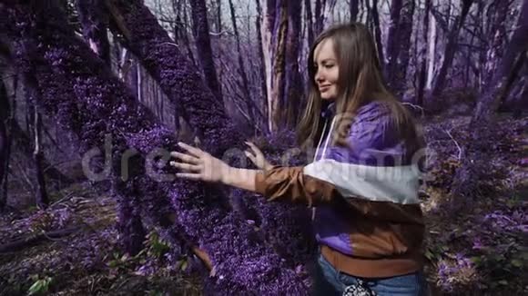 紫罗兰童话森林美丽快乐的女孩在阳光明媚的日子里抚摸着一棵树干树干上长满了厚厚的紫色苔藓视频的预览图