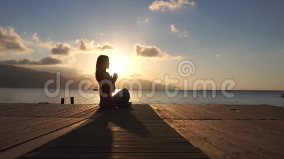 4K一个深褐色的漂亮女孩在日出时在海边慢动作地冥想视频的预览图