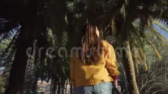 在一个温暖阳光明媚的日子里女孩慢慢地走在厚厚的棕榈树下视频的预览图