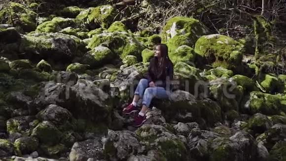 甜美的微笑女孩坐在散落的大石头中间上面长满了绿苔视频的预览图