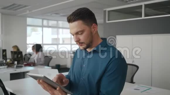 年轻的微笑商人用平板电脑看着镜头微笑他的创意团队正在视频的预览图