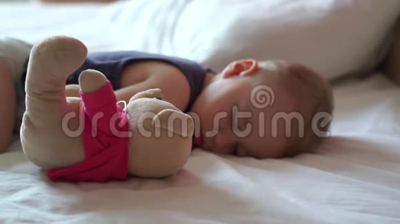 可爱的宝宝慢腾腾地和心爱的玩具熊睡在大床上视频的预览图