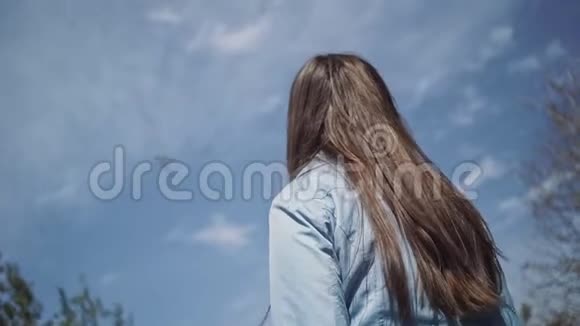 金色长发的女孩抬头望着那架载着云彩在蓝天上飞行的飞机视频的预览图