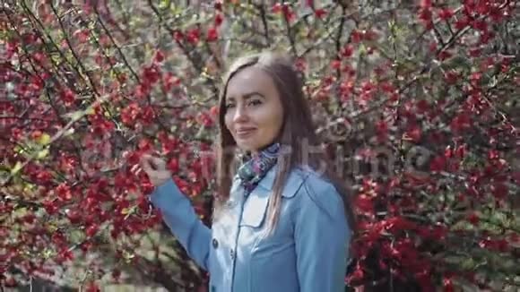 可爱的女孩带着红花离开开花的树在美丽的春天走过公园视频的预览图