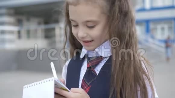 开朗的小学生穿着校服在学校大楼附近的笔记本上写或画一些东西视频的预览图