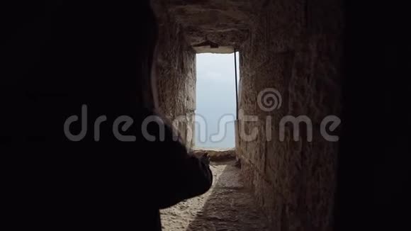 女孩在巨大的城堡墙的一个小窗户里把她的手从黑暗中伸向太阳视频的预览图