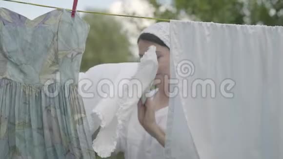 肖像疲惫可爱成熟的女人挂着白色的衣服在晾衣绳上看着户外的相机华盛顿女士在做什么视频的预览图