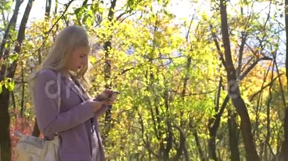 金发商务女孩与智能手机停留秋季森林公园花园技术自然美丽幻想自然视频的预览图
