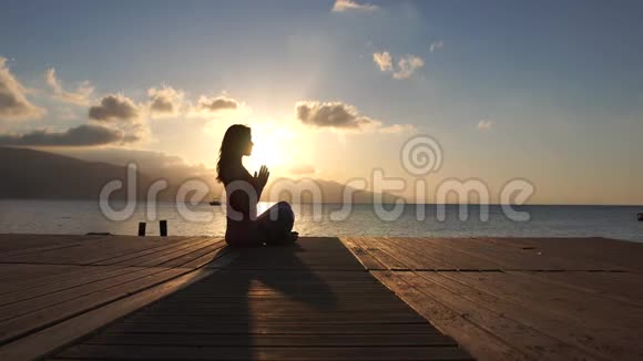美丽的运动女孩在日出时缓慢地在海边祈祷视频的预览图