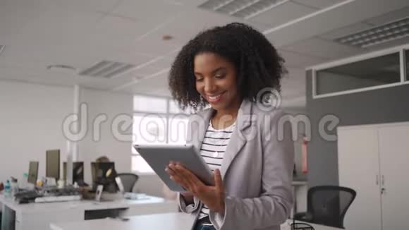 成功微笑的年轻非洲女商人身穿灰色夹克在同事面前使用数字平板电脑视频的预览图