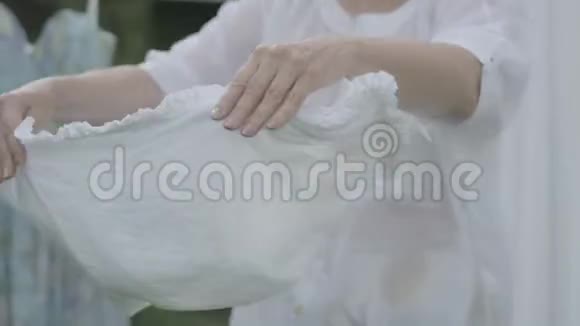 一位迷人的女人留着长发黑发把白色的衣服挂在户外的晾衣绳上洗衣日视频的预览图