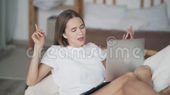 女孩坐在带笔记本电脑的草椅上用无线耳机听音乐跳舞视频的预览图