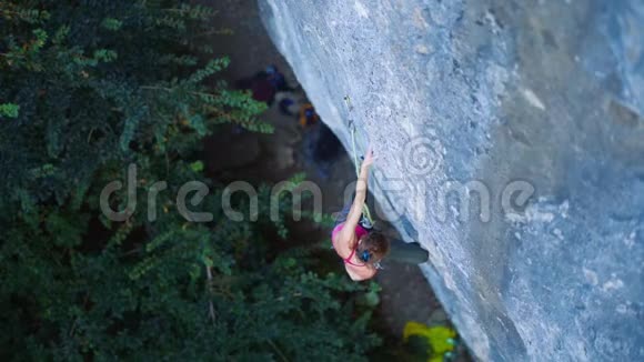 俯视女子攀岩者在艰难的运动路线上攀爬攀岩者休息粉笔手挂在悬崖上视频的预览图