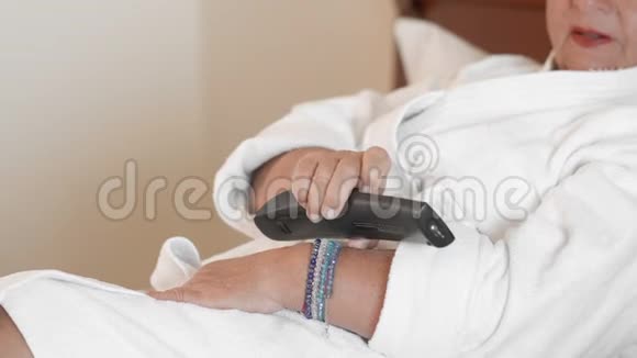 未被认出的女人躺在酒店的床上穿着白色浴袍用遥控器控制电视的概念视频的预览图