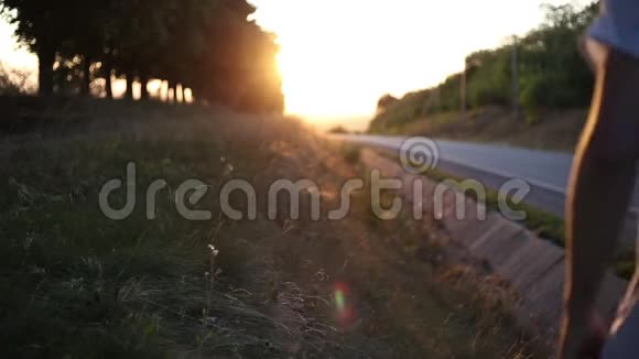 在柏油路附近的日落时分背着背包在草地上散步的年轻人视频的预览图