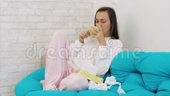 生病的年轻女子坐在沙发上在家里用纸纸吹鼻子视频的预览图