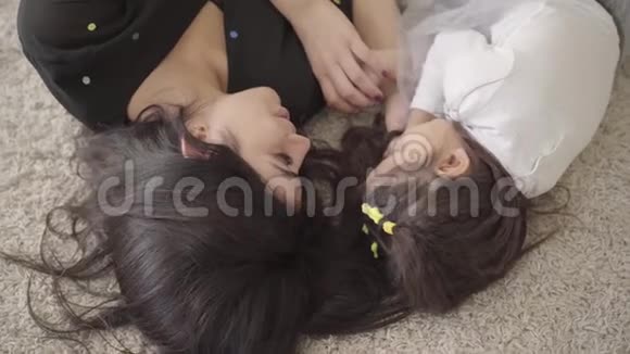 一位美丽的中东年轻女子和她的女儿躺在柔软的地毯上交谈的肖像快乐的母亲视频的预览图