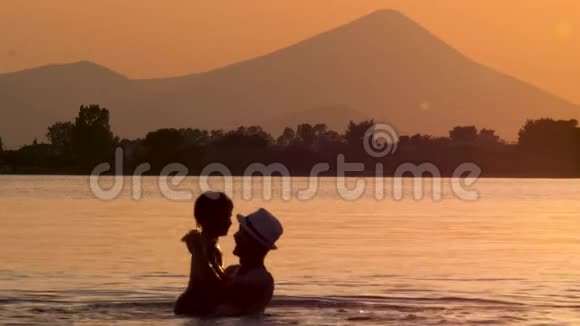 父母带着孩子在海中玩耍背景是山日落时分的尖山集中在快乐的父亲身上视频的预览图