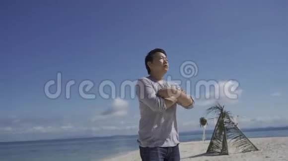 亚裔泰国男子站在沙滩上镜头在他周围移动视频的预览图