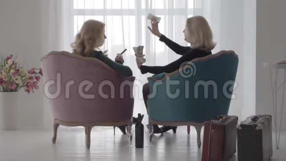 回到富有的高加索女人坐在舒适的扶手椅和吝啬的钱高级女性支出视频的预览图