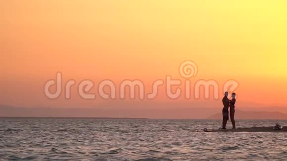 日落时一对夫妇在海滩上拥抱的剪影橙色的天空视频的预览图