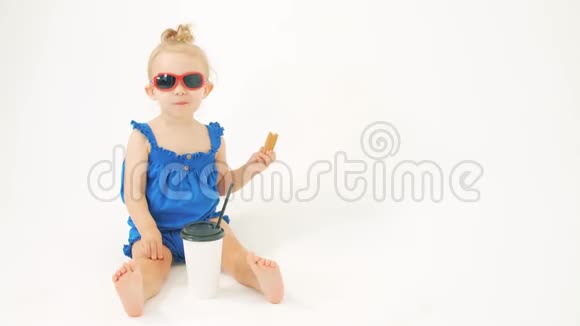 一幅女婴戴着太阳镜穿着蓝色连衣裙在白色背景下吃零食的肖像视频的预览图