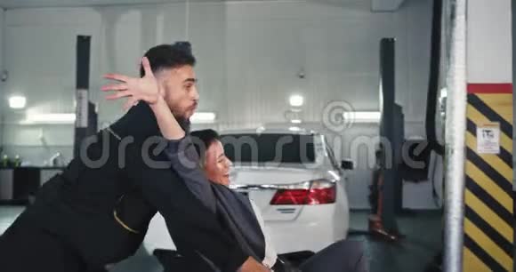 在一个现代化的汽车车库里镜头前的帅哥和一位坐在摇椅上的顾客小姐玩得很开心视频的预览图