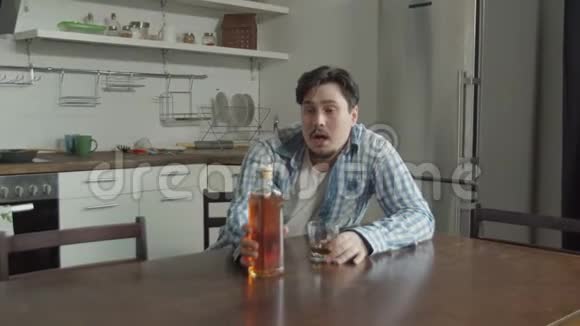 在家庭厨房悲伤地喝酒的男人视频的预览图