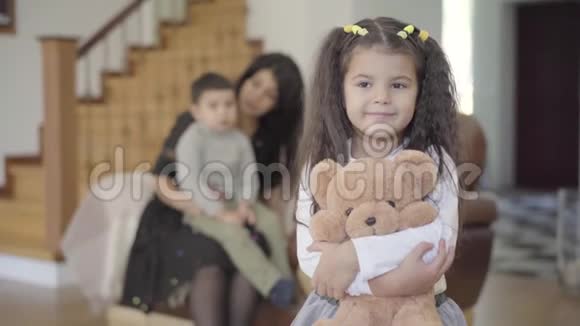 微笑中东女孩棕色的眼睛和卷曲的头发拿着泰迪熊看着相机儿童视频的预览图