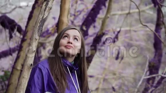 紫罗兰童话森林穿着彩色夹克的可爱女孩正看着童话故事中不寻常的苔藓覆盖的树木视频的预览图