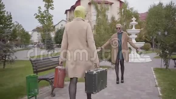 两个成熟的高加索女性朋友在旅行期间见面优雅的女人带着两个旅行袋走向微笑视频的预览图