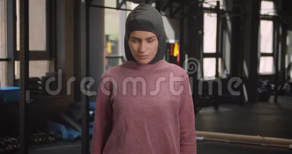 年轻漂亮的运动穆斯林女性特写镜头看着镜头兴高采烈地站在室内健身房视频的预览图
