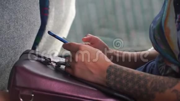 手臂上有纹身的女孩在公共交通工具中使用智能手机视频的预览图