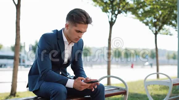 不高兴的商人智能手机在街上的长凳上读坏消息不良销售代理证券交易所视频的预览图