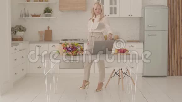 快乐的金发白种人女士站在现代厨房里端着一杯茶或咖啡和一束花快乐视频的预览图