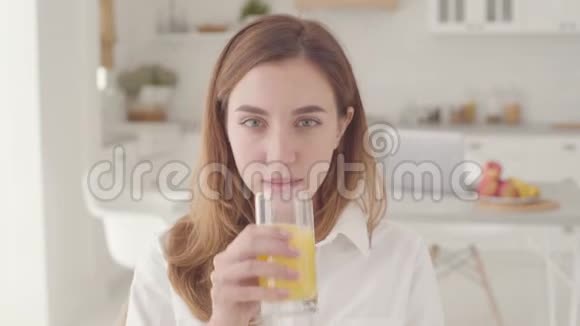 一位年轻美丽的白种人女人的特写脸品尝着橙汁满意地微笑着很漂亮的笑容视频的预览图