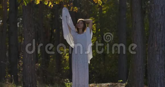 美丽微笑的白种人女孩站在森林里戴着被风吹过的浅白色围巾抬头看着美丽美丽视频的预览图