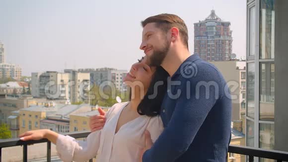 年轻的白种人夫妇相爱拥抱和亲吻在露台上享受城市景色视频的预览图