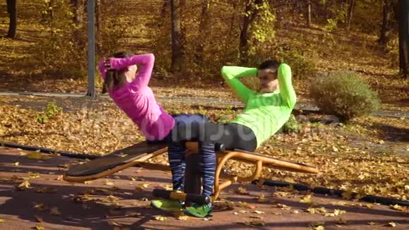 一对年轻夫妇在秋季公园的运动场上做腹部运动视频的预览图