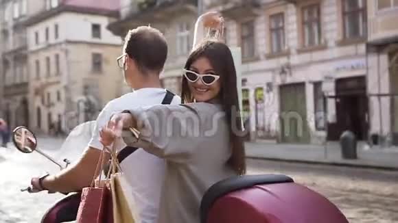一位微笑的年轻女士手里拿着购物包骑着滑板车和她的男性朋友骑着滑板车动作缓慢视频的预览图