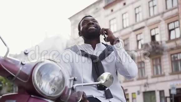慢动作赢得非裔美国人男子与愉快的微笑在电话交谈坐在美丽的滑板车上视频的预览图